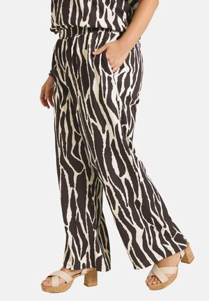 Kvinde iført sort-hvide zebrastribede bukser med vidde ben og beige kork platformssandaler med krydsede remme. Den ene hånd i lommen.