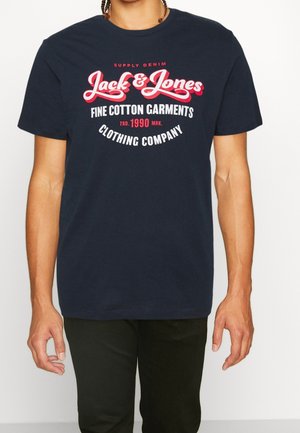 Mężczyzna w granatowej koszulce Jack & Jones z białym i czerwonym napisem o wysokiej jakości bawełnianych ubraniach i firmie odzieżowej.