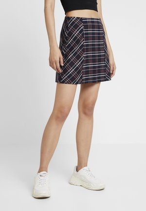 Minifalda de cuadros azul marino con acentos en rojo y blanco, con cintura ajustada y forma acampanada. Combinada con zapatillas blancas gruesas.