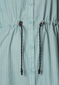 Indumento blu chiaro con strisce verticali nere, bottoni frontali e un cordoncino nero con puntini bianchi e terminali metallici in vita.