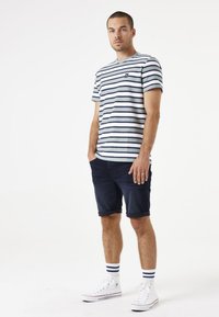 Camiseta de manga corta a rayas en azul claro y marino, combinada con pantalones cortos de mezclilla oscuros. Zapatillas blancas con calcetines a rayas en azul marino completan el look.