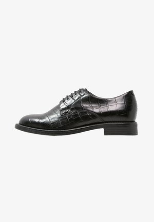 Chaussure habillée pour homme en cuir noir avec motif crocodile, fermeture à lacets et petit talon empilé, montrée en profil latéral sur fond blanc.