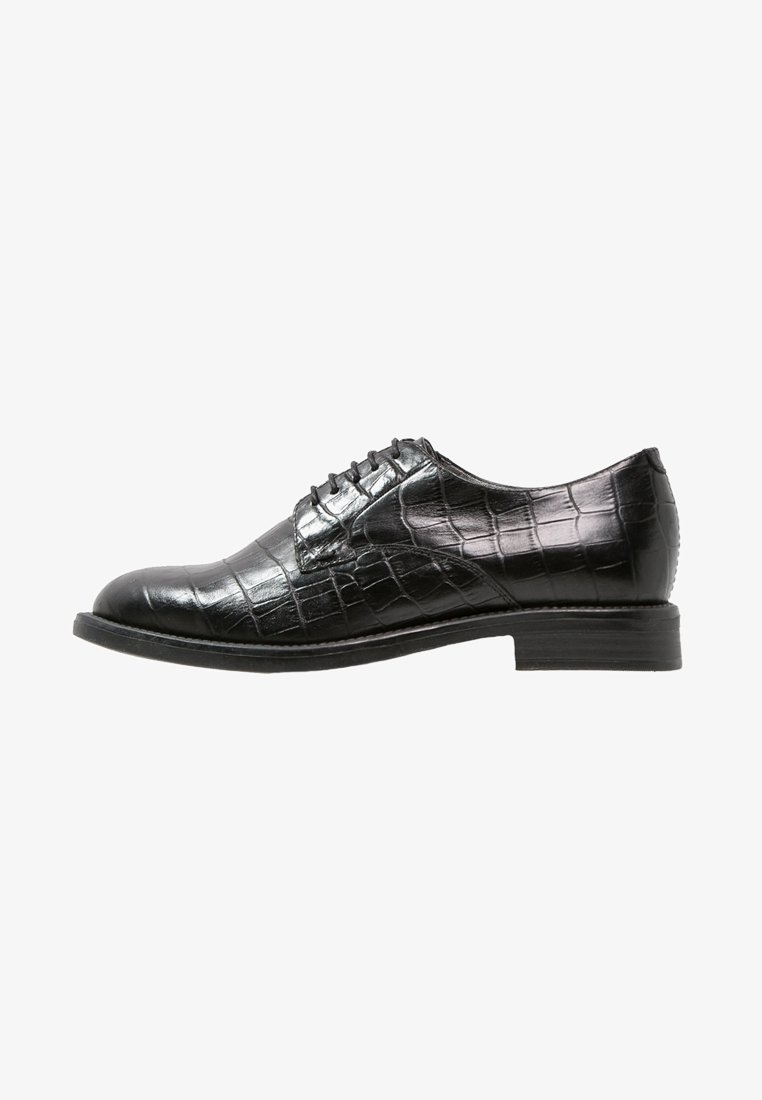 Chaussure habillée pour homme en cuir noir avec motif crocodile, fermeture à lacets et petit talon empilé, montrée en profil latéral sur fond blanc.
