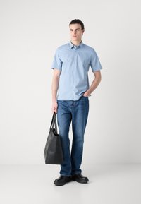 Világoskék, rövid ujjú, gombos ing, melyet kék farmernadrággal párosítanak. A modell egy fekete kézitáskát tart, és fekete lábbelit visel. Egyszerű dizájn, laza megjelenés.