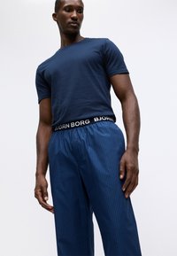 Navy plava pamučna majica s kratkim rukavima, u kombinaciji s plavim prugastim pidžama hlačama sa crnim pojasom s natpisom "BJORN BORG."