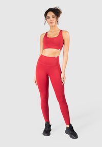 Sujetador deportivo rojo y leggings a juego hechos de material elástico. El sujetador tiene tirantes anchos y los leggings presentan una cintura alta. Zapatillas negras.