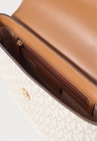 Τσάντα χειρός από υφασμάτινη κρεμ με υφή, με εσωτερικό από καφέ δέρμα, που διαθέτει τσέπη με φερμουάρ και κλείσιμο με στρογγυλό κούμπωμα σε χρυσό τόνο.