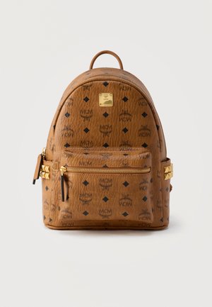 Brown leather MCM backpack with black logo pattern, front zip pocket, gold studs on sides, and a gold brand plaque on top center.