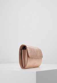 Rosaguld clutchväska med texturerad yta, med en vikbar klaff och en smal design, uppvisad på en vit plattform.