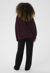 Per didelį bordo megztinį su laisvu siluetu, tekstūriniu audiniu ir nuleistomis petnešomis; derinamas su juodomis plačiomis kelnėmis.