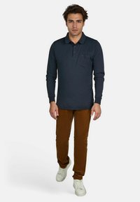 Marineblauwe poloshirt met lange mouwen en een borstzak, gecombineerd met een paar bruine corduroy broek en witte sneakers. Eenvoudig ontwerp en een gladde textuur.