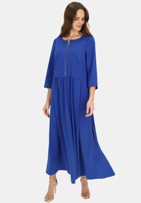 Niebieska, długa sukienka maxi z długimi rękawami, okr�ągłym dekoltem i centralnym złotym zamkiem błyskawicznym. Lekki materiał z marszczonym pasem zapewnia zwiewny fason.