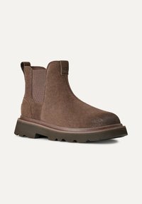 Stivale alla caviglia in suede marrone con pannelli laterali elastici, punta arrotondata e suola in gomma testurizzata con battistrada profondo per una migliore aderenza. Logo UGG sul tallone.