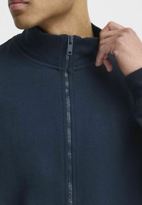 Tengerészeti zipzáras dzseki magas gallérral, struktúrált bordázással és sima szövetfelülettel, ellenkező színű cipzárral.