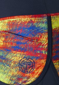 Värikäs uimapuku joustavasta kankaasta, jossa on kirkas keltainen, punainen ja sininen kuvio, logolla alakulmassa ja mustalla vyötärölinjalla.