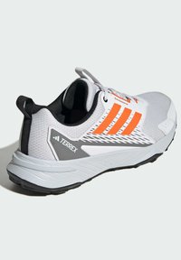 Witte sportieve schoen met oranje accenten, gestructureerde mesh bovenkant, zwarte binnenkant en grijze branding aan de zijkant. Gebogen zool voor ondersteuning.