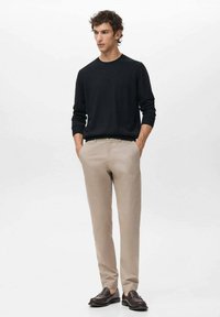 Schwarzer Pullover, beige Hose, braune Schuhe. Der Pullover hat einen Rundhalsausschnitt, und die Hose ist gerade geschnitten mit klaren Linien, was einen minimalistischen Look schafft.
