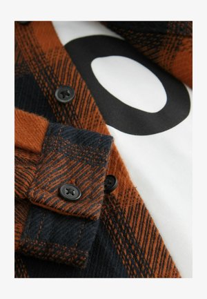 Camisa de franela en naranja y azul marino con un patrón de cuadros, con botones negros y una camiseta blanca debajo que muestra un gráfico en negro audaz.