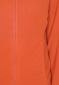Giacca in pile arancione con texture liscia, dotata di chiusura centrale a zip e linee pulite nel design. Tessuto morbido evidente in primo piano.