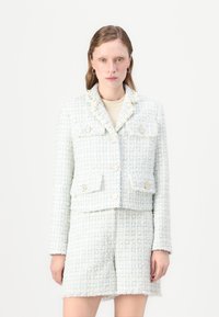 Šviesiai mėlynas tweed blazeris su sutrumpintu siluetu, turintis keturis priekiniai kišenes, auksinius mygtukus ir purvinas galiukus, derinamas su tweed mini sijonu.
