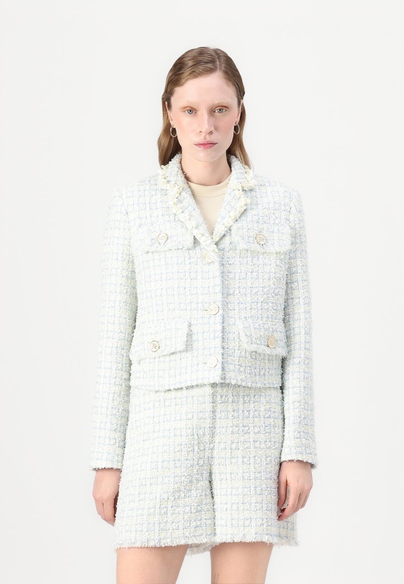 Šviesiai mėlynas tweed blazeris su sutrumpintu siluetu, turintis keturis priekiniai kišenes, auksinius mygtukus ir purvinas galiukus, derinamas su tweed mini sijonu.