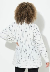 Weißer gestrickter Pullover mit schwarz gesprenkeltem Muster, lockere Passform, lange Ärmel und gerippte Bündchen. Entwickelt für Komfort und Wärme.