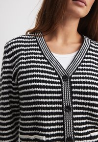 Cardigan rayé noir et blanc avec un col en V, finitions côtelées et fermeture à boutons. Présente un motif de tricot texturé.