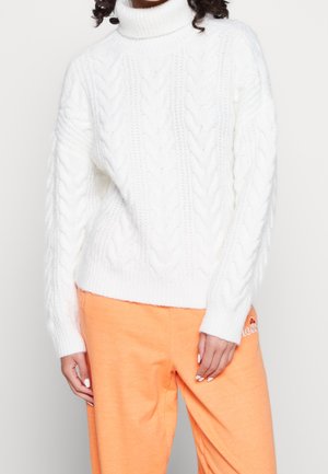 Valkoinen neulepusero, jossa on korkeakaulus ja pujotuskudontakuvio, yhdistetty oranssin värisiin collegehousuihin. Pehmeä rakenne, rento istuvuus.