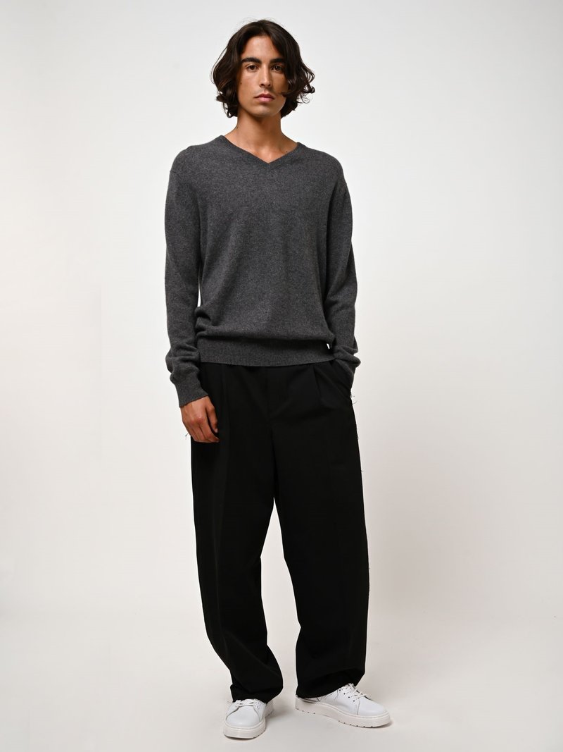 Harmaa V-kaula-aukkoinen neule, joka on valmistettu pehmeästä materiaalista, yhdistettynä löysiin mustiin housuihin ja valkoisiin lenkkereihin. Yksinkertainen muotoilu, minimalistinen ilme.