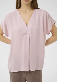 Blusa rosa chiara con scollo a V e maniche corte e larghe. Tessuto morbido con una sottile texture. Presenta una piega centrale per modellare.