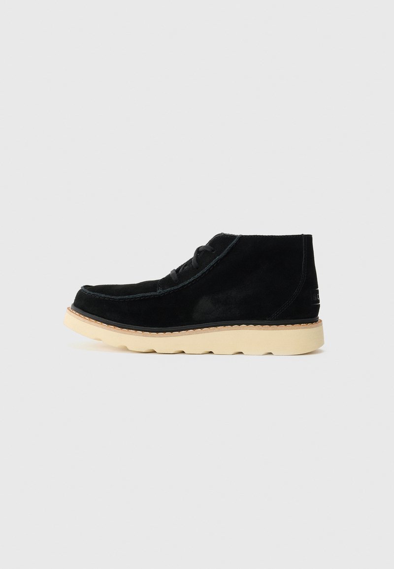 Black suede ankle boot with beige rubber sole, moc toe stitching, and black laces set against a plain light background.