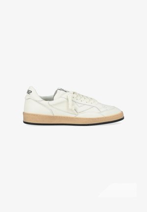 Hvid lædersneaker med en tekstureret tan gummisål, minimal syning, rund tå og flade snørebånd. Har en sort accent på hælen.