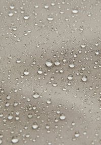 Vattendroppar på en texturerad beige tygyta, som framhäver vattenavvisande egenskaper med varierande storlekar och spridd fördelning.