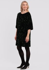 Black sequin dress with batwing sleeves, knee-length, features a textured surface, and is paired with black tights and high-heeled shoes.