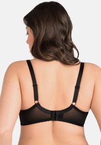 Black bra with adjustable straps, sheer paneling, scalloped edges, and a hook-and-eye closure at the back. Textured fabric.