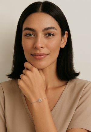 Bracciale d'argento con un pendente circolare che presenta un design ad albero, indossato su un polso di carnagione abbronzata. La camicia è beige con un design a scollo a V.