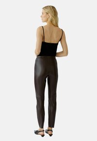 Zwarte mouwloze top, hoog opschortende bruine leren broek met een gladde textuur, aansluitend ontwerp; gedragen met zwarte instappers.