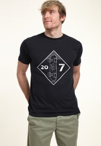 Černé tričko s krátkým rukávem s bílou diamantovou grafikou se čísly 20 a 7 a ilustrací skateboardu uprostřed.