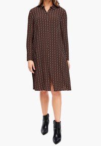Šaty s dlouhým rukávem a knoflíkovým zapínáním, zdobené geometrickým vzorem v hnědé, krémové a černé barvě. Materiál má hladkou texturu a vp�ředu je rozparek.