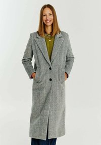 Kabát s herringbone vzorem v černé a bílé barvě, s dlouhým střihem, klopami se zářezem, dvěma předními kapsami a dvěma černými knoflíky.