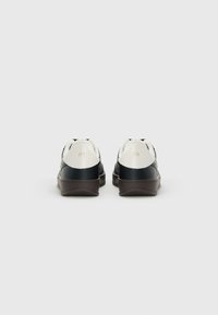 Een paar zwart-witte lage sneakers, gezien vanuit de achterkant op een effen lichte achtergrond.