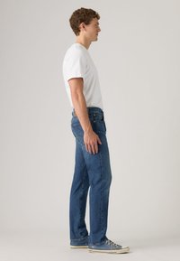 Blue denim jeans with a straight fit, featuring stitched seams, five-pocket design, and a leather brand patch on the back waistband.