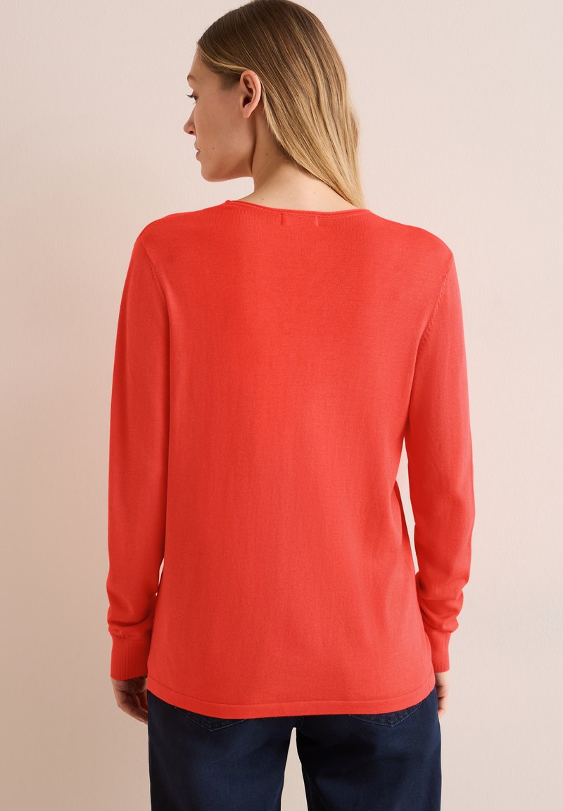 Czerwona longsleeve sweter z okrągłym dekoltem, gładką fakturą i ściągaczami przy mankietach. Tył ma prosty wzór i prosty dół.