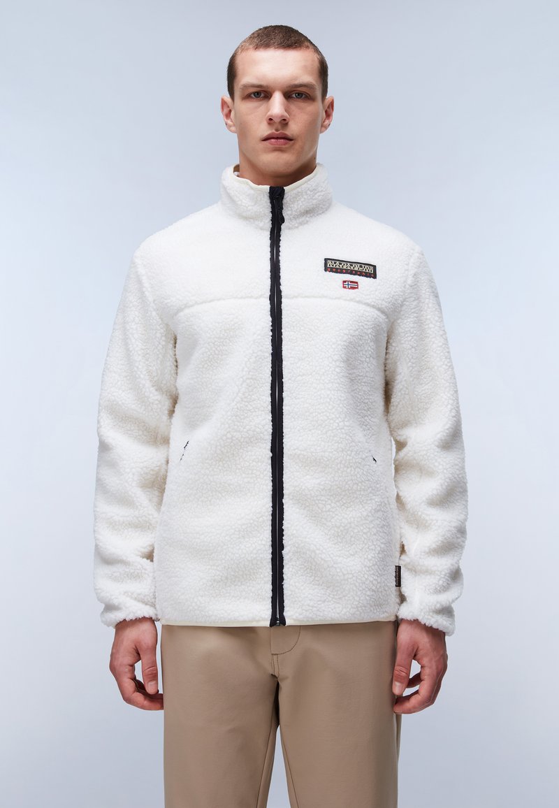 White fleece jacket with a high collar, black zip closure, and logo patch. Features textured fabric and side pockets.