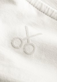 Witte stof met een getextureerd, geborduurd schaarlogo in een subtiele, bijpassende draadkleur. Gladde oppervlakte met een fijne weving.