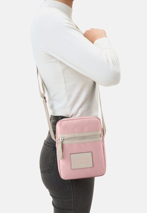 Rosa Umhängetasche aus weichem Material, mit einer vorderen Reißverschlusstasche, einem beigen Akzentlabel und einem schmalen verstellbaren Trageriemen.