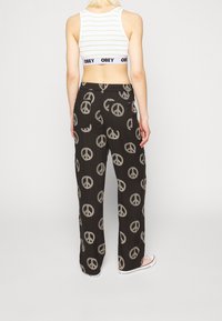 Schwarze Hose mit einem Friedenzeichenmuster in Beige. Lockere Passform mit einem elastischen Bund. Getragen mit einem weiß gestreiften Cropped-Top.