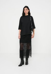 Black top with short sleeves and a loose fit, paired with a long black lace skirt, featuring a textured pattern. Worn with chunky black boots.