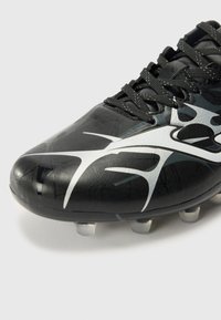 Scarpa da calcio nera con superficie texturizzata, caratterizzata da un design astratto bianco, lacci neri e tacchetti traslucidi sulla suola.