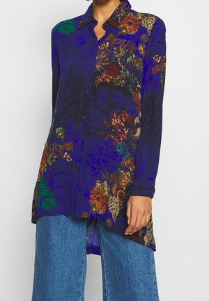 Langärmliges Hemd mit Knopfleiste, tiefblauem Grundton und mehrfarbigen Blumen- und Pflanzenmustern, kombiniert mit blauen Jeans aus Denim.